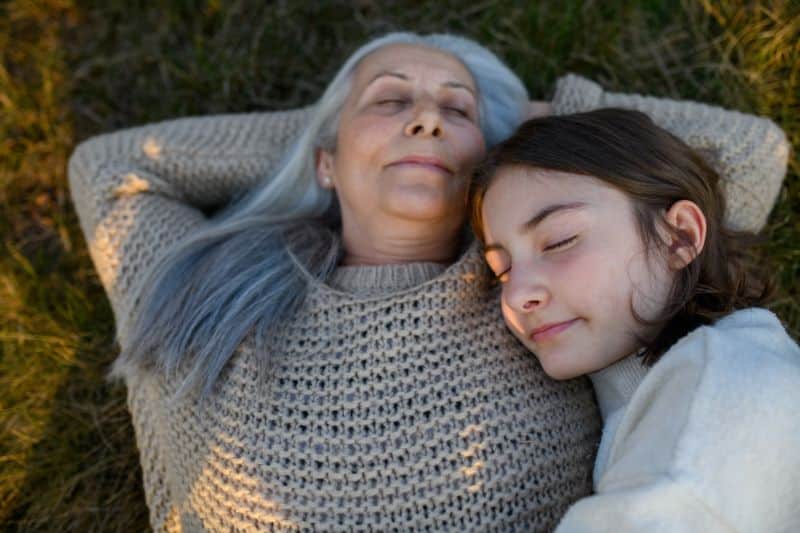 happy grandmother with teen granddaughter both laying in grass