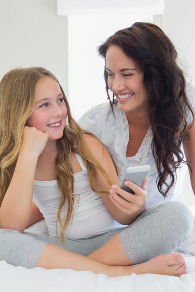 mother and young daughter smiling at each other, daughter holding mobile phone