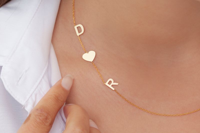 necklace on woman's neck with initials D and R along with a heart