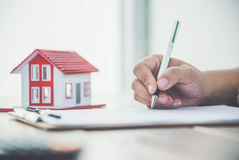 signing contract for home, miniature house beside clipboard