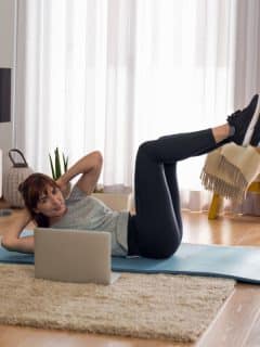 woman doing crunches on floor with laptop in front