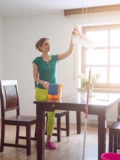 woman dusting light fixture over table
