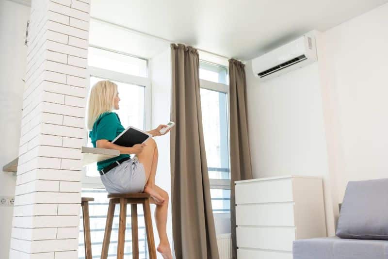 woman pointing remote control at air conditioner
