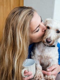 woman holding coffee and dog, kissing dog