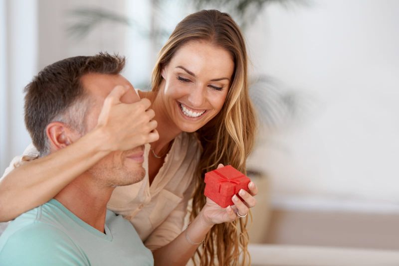 woman surprising her husband with a gift in a small red box