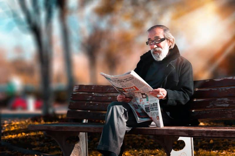 elderly man reading newspaper on bench