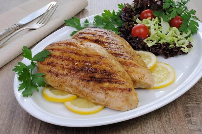 grilled chicken on white plate with salad and lemon slices