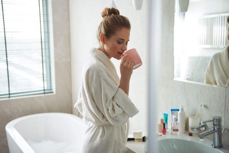 woman enjoying hot cup of tea while filling a tub