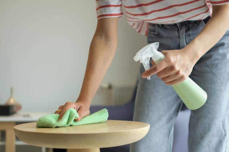 woman cleaning a small table with a green cloth