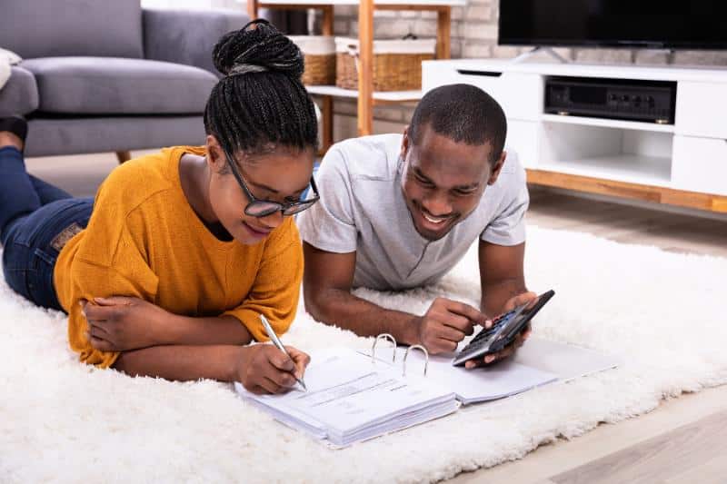 couple laying on fuzzy white rug while working on budget