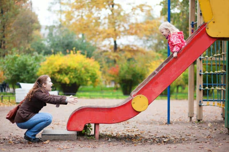 mother with open arms to catch daughter going down slide