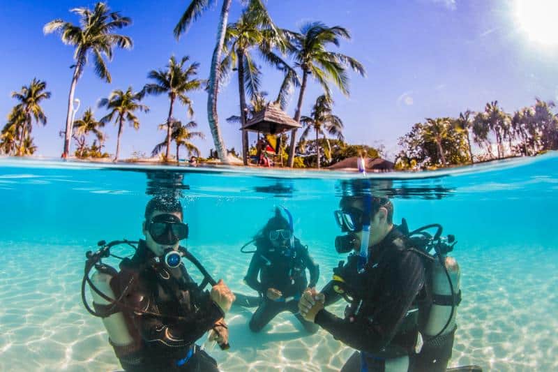 two men and one woman scuba diving in shallow water