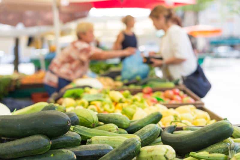 veggies in foreground with farmers market shoppers in background