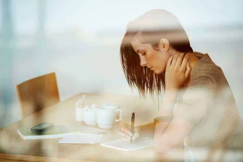 woman sitting at a table alone writing in a journal