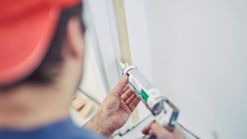 man applying caulk to a door