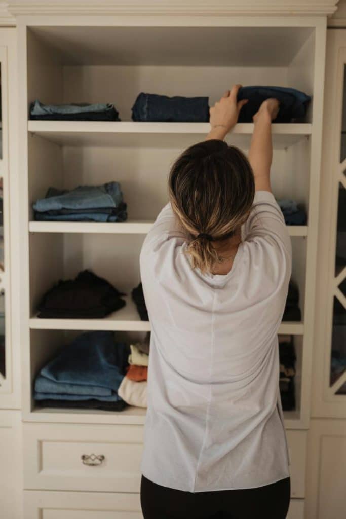 woman putting clothes on shelves in closet