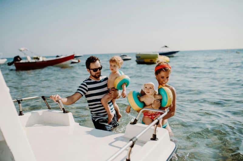 family with toddlers in water near a boat