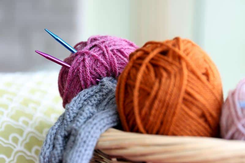 colorful balls of yarn and knitting needles in basket