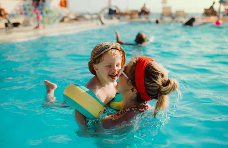 mom holding toddler son in pool while he's wearing arm floaties