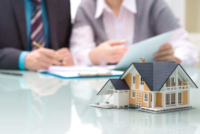 model of a house in foreground and people signing contract in background