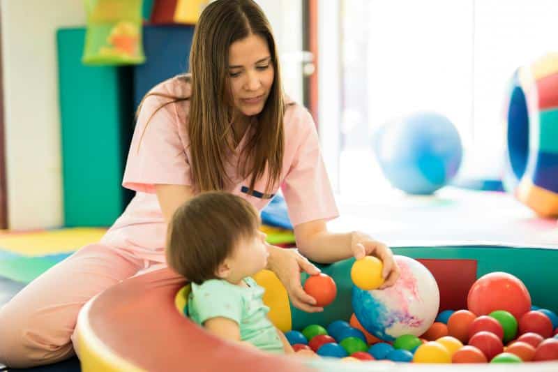physical therapist working with baby in ball pit