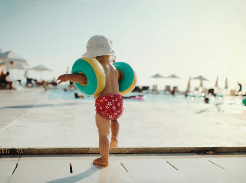 toddler in swim diaper, bucket hat, and arm floats
