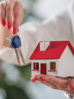 woman holding a small model of a house in one hand and keys in another