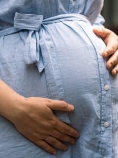 woman's hands holding her pregnant belly in blue shirt