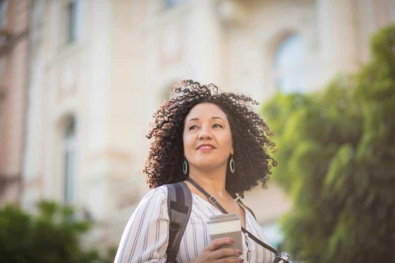 woman standing in street in front of building holding coffee