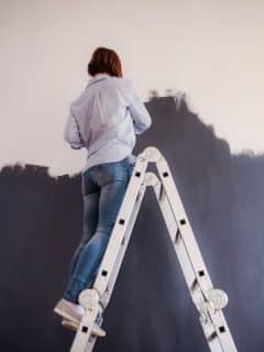 woman on ladder painting wall black