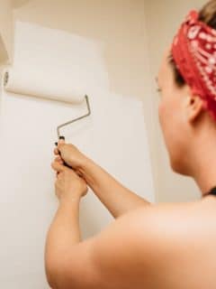 woman painting wall white using a paint roller