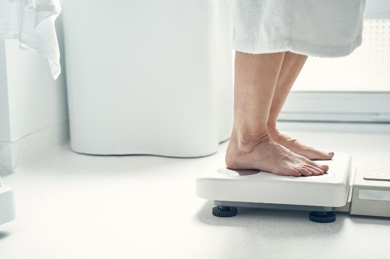 woman standing on a scale in a white bathrobe - only legs and feet visible