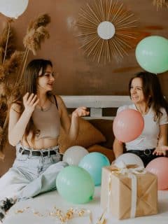 women sitting on a bed with balloons and a gift