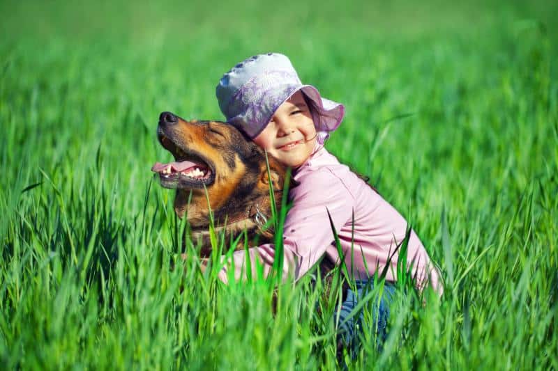 girl in tall grass hugging dog