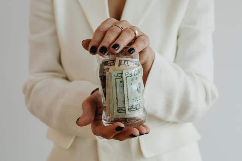 woman in white blazer holding jar of money