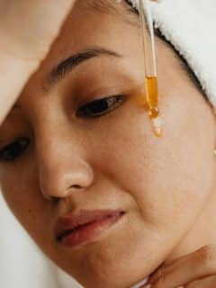 woman with towel on head applying serum to face using an eye dropper