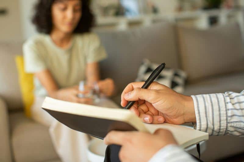 woman talking in background while someone writes in a notebook in foreground