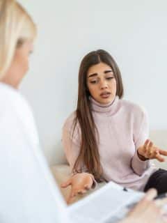 woman sitting on sofa talking while therapist takes notes