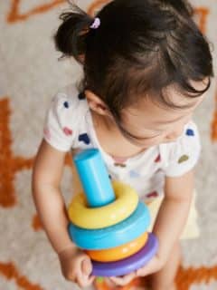 toddler girl carrying a stacking toy