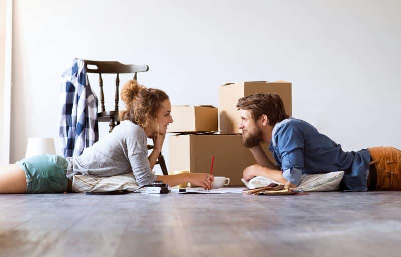 young couple on floor looking at each other with moving boxes in the background