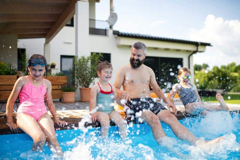 dad and three daughters splashing feet in the pool