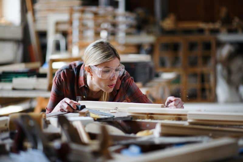 woman blowing sawdust off a board in a wood shop