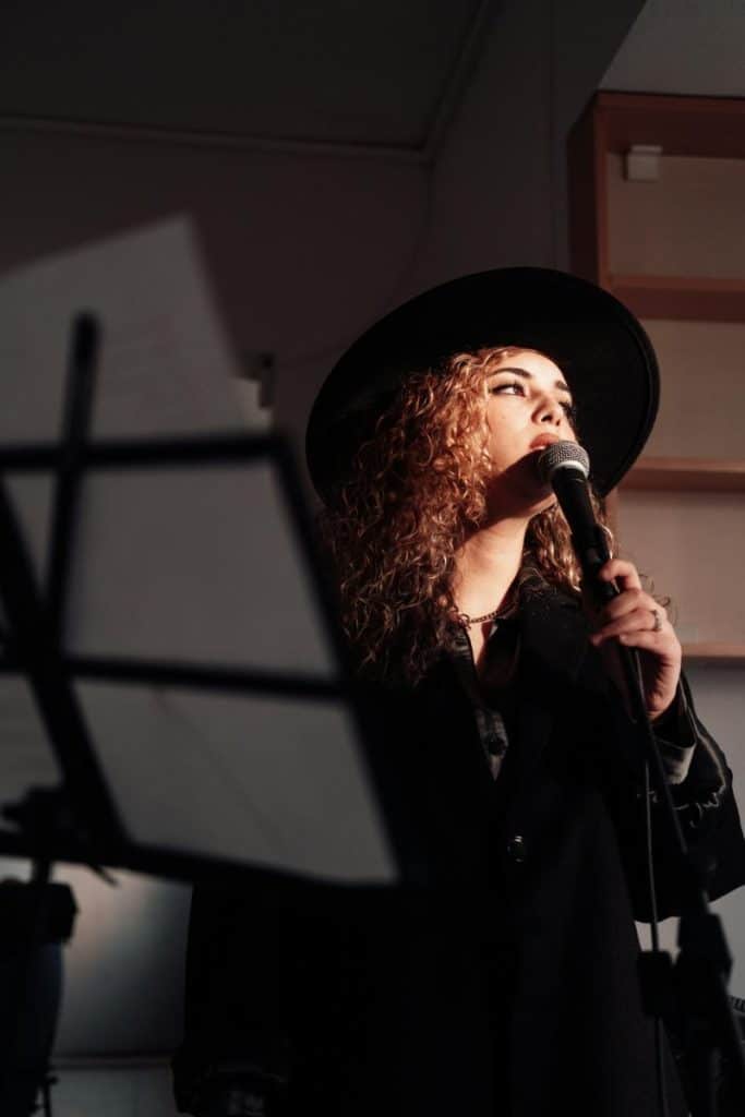 female singer with curly hair and black hat holding a microphone