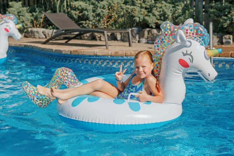 girl with red hair on unicorn float and holding up fingers in peace sign