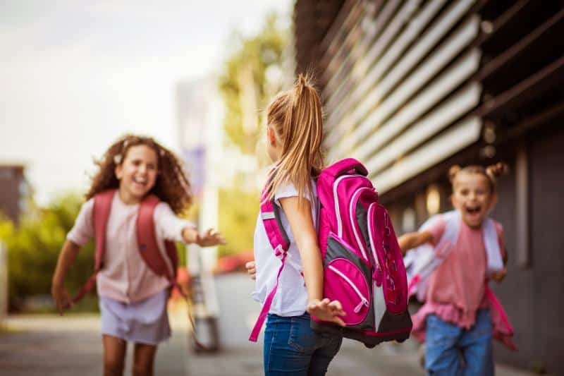 young girls running outside school, all with backpacks on