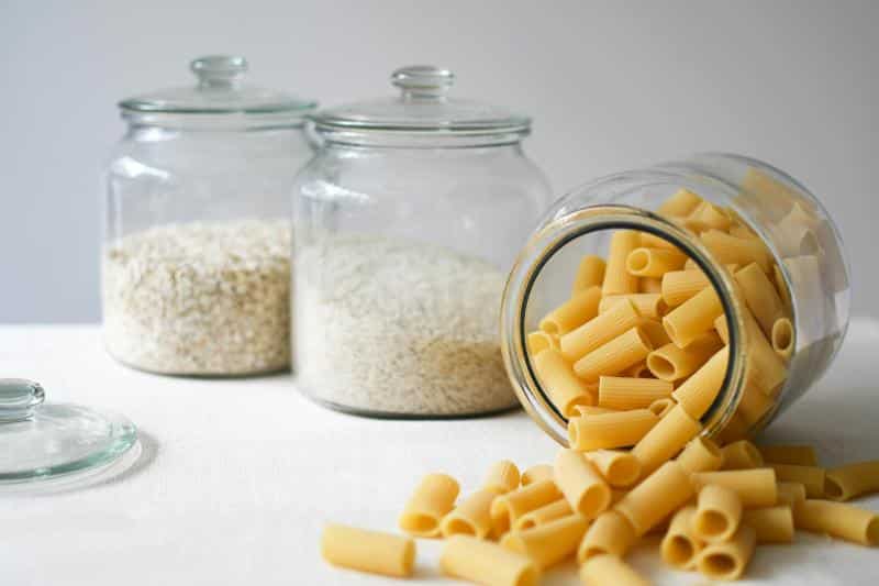 food containers with oats, rice, and pasta - the jar with pasta is open and spilling out