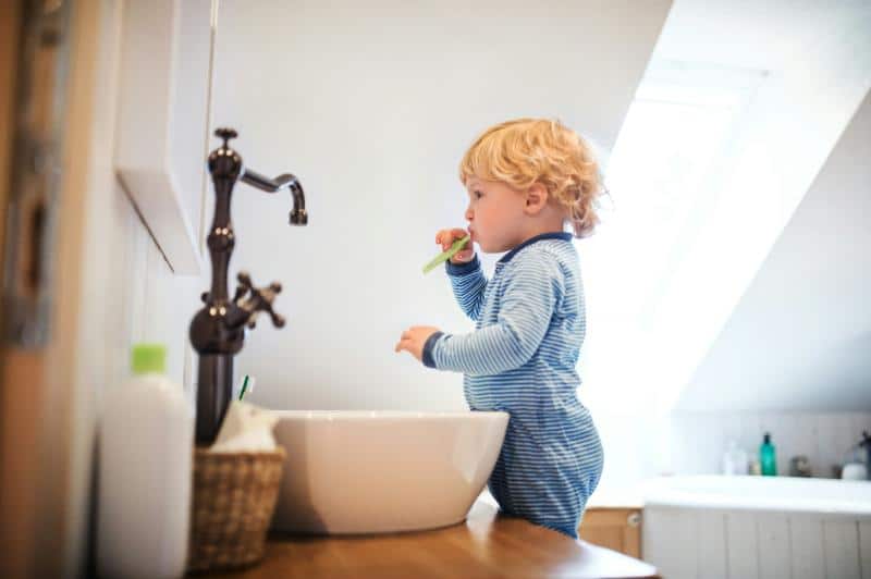 toddler boy brushing teeth at sink while looking in mirror