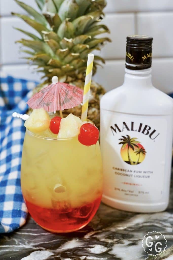 Malibu Sunset layered cocktail garnished with cherries and pineapple