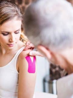 senior man applying physiotherapy tape to a blonde woman's shoulder