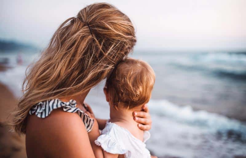 mom holding baby on beach, faces away from the camera